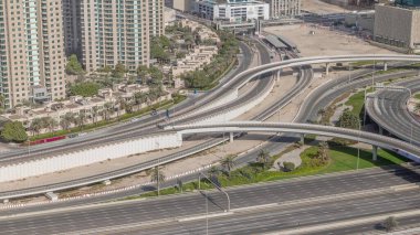Dubai Marina 'da büyük bir karayolu kavşağında hava manzarası var. Etrafında da İHA' lar var. JLT bölgesinden araba trafik görüntüsü. Yeşil çimenler ve palmiyeli ağaçlar