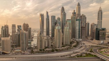 Dubai Marina karayolu kavşağı spagetti kavşağı akşam saat dilimi. Cam yüzeyinde güneşin yansıması olan en uzun gökdelenler. Gün batımında bulutlu turuncu gökyüzü ile JLT bölgesinden hava manzarası