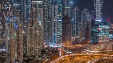 Dubai Marina 'da büyük bir karayolu kavşağında hava manzarası var. Çevrede gökdelenler var, BAE. JLT bölgesinden araba trafik görüntüsü. Pencerelerinde ışık olan aydınlık kuleler