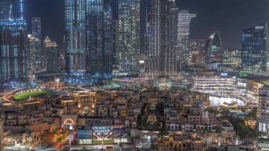 Gökdelenlerle çevrili eski kasaba adasının aydınlatılmış geleneksel evlerinin gökdelenlerle dolu gece manzarası. Dubai şehir merkezinde alışveriş merkezi ve çarşıya yakın çeşme alanı var.