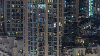 Modern konut binalarındaki büyük parlayan pencereler geceleri zaman ayarlı, sıra sıra parlıyor. Çatı bahçesi.