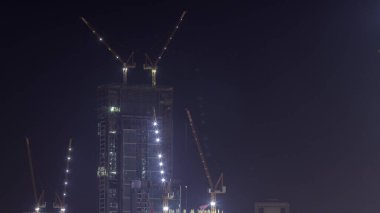 İnşaat halindeki çok katlı binalar ve gece vakti vinçler. Yeni kuleler ve gökdelenlerin hava manzaralı inşaat sahasında aktif iş