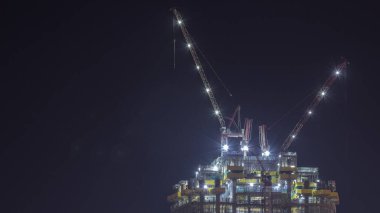 İnşaat halindeki çok katlı bir bina ve gece vakti vinçler. Yeni gökdelenin şantiyesinde aktif çalışma.
