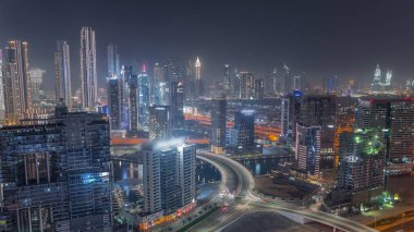 Dubai iş sahasının modern mimarisi ile Skyline ve finans bölgesi zaman çizelgesi üzerine aydınlatılmış kuleler. Kanal ve şantiyeli hava manzarası