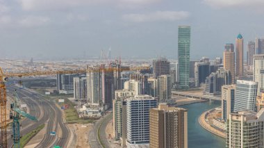 Dubai iş sahası kulelerinin modern mimarisi ve karayolu üzerindeki trafiği gösteren bir siluet. Kanallı hava manzarası ve vinçli inşaat sahası