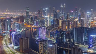 Dubai iş sahasının modern mimarisi ile Skyline birçok aydınlatılmış kule gece zaman çizelgesi. Kanal ve şantiyeli hava panoramik görüntüsü