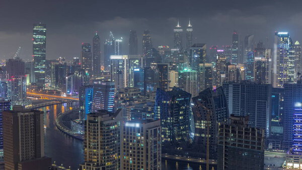 Skyline with modern architecture of Dubai business bay illuminated towers night timelapse. Aerial view with canal and construction site