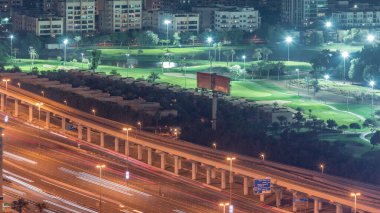 Aydınlatılmış golf sahasının havadan görünüşü yeşil çimenler ve göller, arkasındaki villa evleri gece zaman atlaması. Otoyol trafiği. Dubai marina gökdeleninden en iyi manzara.