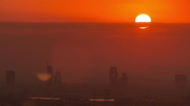 Sebze üzerinden gün doğumu ve Dubai marinasından Al Barsha Tepeleri hava zaman çizelgesi. Golf sahasının yakınındaki kulelerin ve gökdelenlerin arkasından güneş yükseliyor.
