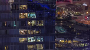 Modern ofisteki pencere ışıkları ve geceleri konut binaları. İçinde aydınlık odalar olan çok katlı gökdelenler. Arkadaki yolda trafik vardı.