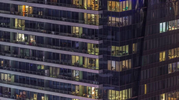 Modern ofisteki pencere ışıkları ve geceleri konut binaları. İçinde aydınlık odalar olan çok katlı gökdelenler. Balkonda birileri var.