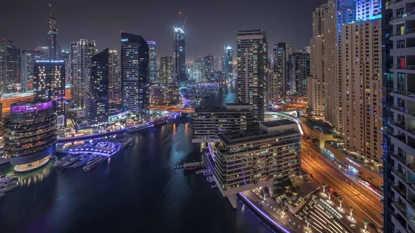 Dubai marinasına giden hava manzaralı gökdelenler ve kanalın etrafındaki JBR kuleleri gece saatlerinde yüzen yatlarla aydınlatıldı. Yat kulübünde beyaz tekneler var.
