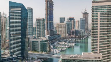 Kanal çevresindeki Dubai marina gökdelenlerine doğru yüzen botların zaman ayarlı görüntüsü. Yat kulübünde beyaz tekneler var.