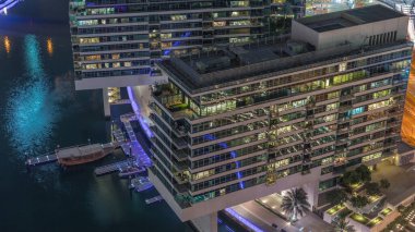 JBR ve Dubai Marina 'ya genel bakış. Rıhtımda yaşayan apartmanlardaki modern binaların gökyüzü. Gece saatleri. Sudaki tekneler ve pencerelerdeki akşam ışıkları