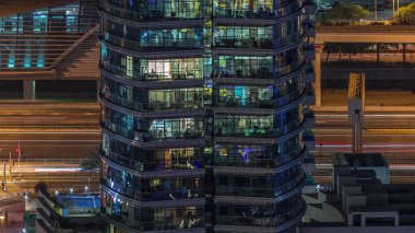 Gece vakitlerinde apartmanların pencereleri, evlerin pencerelerinden gelen ışık. Parlak odalı şehrin akşam manzarası. Gökdelenin arkasındaki trafik