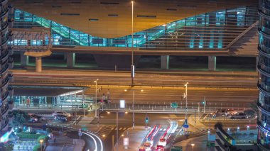 Tramvay durağı yakınlarındaki trafik ve metro istasyonundan çıkış Dubai marinasında bir arka planda gece uçuşu zaman aralığı. Otoyol çevresindeki gökdelenler