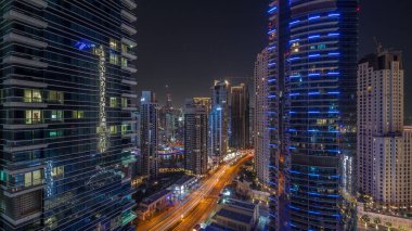 Dubai Marina ve JBR bölgesinin panoramik hava görüntüsü ve tüm gece boyunca yol trafiği. Aydınlatılmış gökdelenler ve ışıklar sönerken