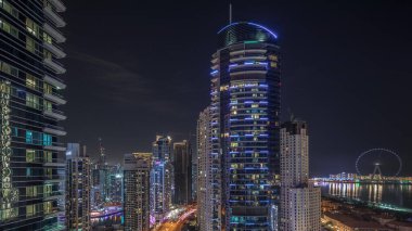 Dubai Marina ve JBR bölgesinin panoramik manzarası ve ünlü dönme dolap gece zaman çizelgesi ve karanlık gökyüzüne karşı aydınlatılmış gökdelenler.