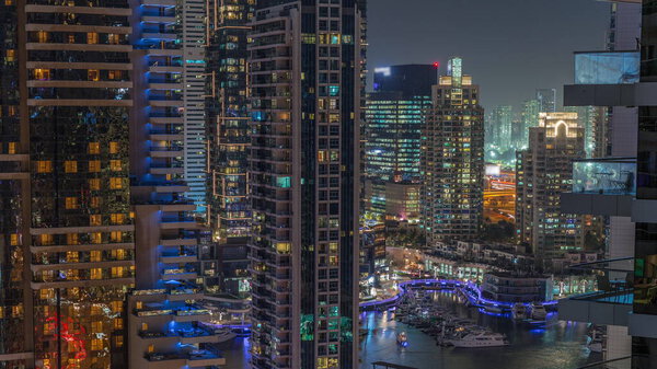 Aerial view on Dubai Marina illuminated skyscrapers and the most luxury yacht in harbor night timelapse. Towers along walking area on a waterfront. Dubai, United Arab Emirates