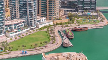 Rıhtım kenarındaki eski ahşap gemi, palmiyeler ve yeşil çimenli havadan zaman ayarlı. Dubai Marina 'da Dhow gezisi, Birleşik Arap Emirlikleri