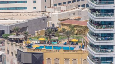 Gökdelenlerin yakınındaki çatı yüzme havuzu. Dubai marinasının havadan görünüşü. İnsanlar şemsiyelerin altında yüzüyor ve dinleniyorlar. Dubai, BAE