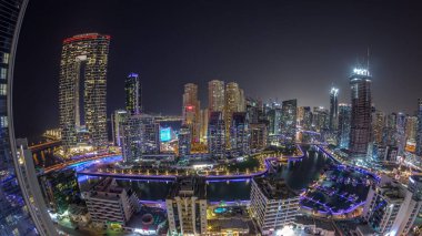 Dubai Marina Panoraması 'nda limana parkedilmiş birkaç tekne ve yat ve Kanal Havalimanı etrafında aydınlatılmış gökdelenler var. Arka planda JBR bölgesi kuleleri