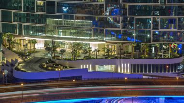 Gece vakti Dubai marinasından gezinti güvertesi ve avuçlar görünüyor. Otel ve gökdelenlerin girişi olan JBR bölgesine hava görüntüsü.