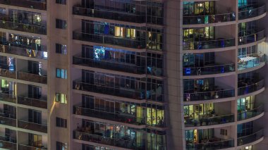 Dışarıdaki apartmanın gece manzarası renkli zaman çizelgesi. Pencerelerinde parlayan ışıklar olan yüksek katlı bir gökdelen. Işıklar cam yüzeyden yansıyor