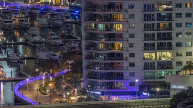 Birçok yat ve tekne limanda gökdelenin arkasında parlayan pencereli gece saatleri ile park halindedir. Dubai Marina rıhtımı yürüyüş alanı. Modern tekne köprünün altındaki derede trafiğe takıldı.
