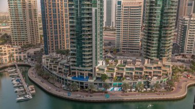 Dubai Marina Havaalanı 'nda palmiyeler ve birçok kafeyle rıhtım gezintisi. Yatlar ve tekneler suda yüzüyor.