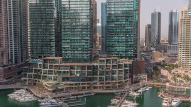 Dubai Marina 'da avuçiçi avuçlarla rıhtım gezintisi. Yatlar ve kayıklar suyun üzerinde yüzer ve arka planda yüksek gökdelenler