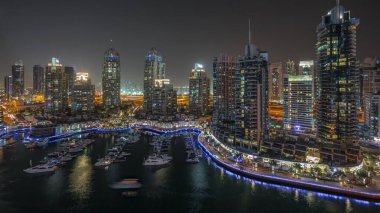 Dubai marinasındaki havadan gece saatlerinde lüks yat körfezi panoraması. Rıhtım boyunca modern gökdelenler ve limanda yüzen tekneler.