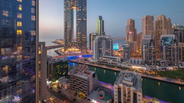 Günbatımından sonra Dubai Marina gökdelenleri ve JBR semti aydınlanmış lüks binalar ve gece geçiş zamanlarıyla dolu tatil köyleri. Palmiyeler ve kanalda yüzen teknelerle dolu bir liman.