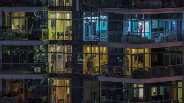 Çok katlı binaların büyük pencerelerinde, çok renkli ışıklardan oluşan düz bir panorama. Büyük bir şehirde aydınlık bir gökdelen.