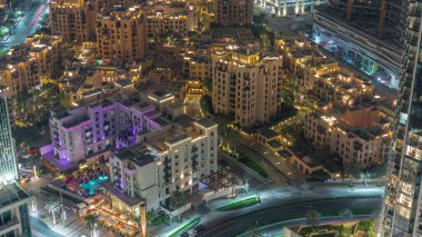 Gökyüzü manzarası, eski kasaba adasının aydınlatılmış geleneksel küçük evlerinin gece zaman çizelgesine yukarıdan bakıyor. Dubai şehir merkezinde sokak trafiği ve ağaçlarla