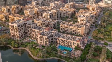 Yeşiller bölgesindeki alçak katlı binalar ve Barsha Heights bölgesindeki gökdelenler. Gün batımında palmiyeler ve ağaçlarla Dubai silueti