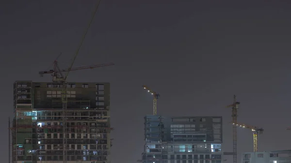 Tall buildings under construction and cranes in downtown night timelapse. Work progress at construction site of new towers and skyscrapers.