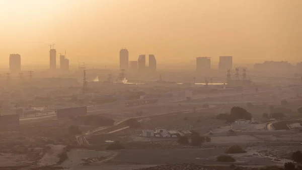 Dubai skyline with villa houses and construction site of new towers on a background orange sky aerial timelapse during foggy sunrise. Desert road with empty area from above
