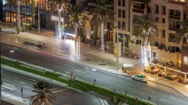 Dubai şehir merkezindeki yolda yoğun bir trafik var. Hava gece saatleri. Aydınlatılmış avuç içleri ve restoranları olan bir bulvar. Birçok araba karşıya geçiyor, BAE