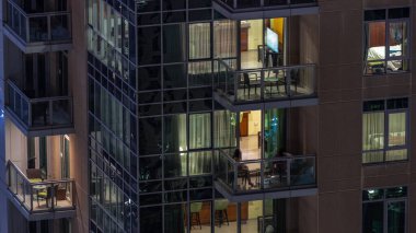 Apartman binasındaki parlayan panoramik pencerelerin gece görüşü. Odalarında ışıklar olan yüksek gökdelenli.