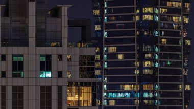 Gece karanlığa bürünmüş gökdelenin panoramik pencereleri şehrin ışıklarının yansımasıyla parlıyor. Aydınlatılmış kuleler