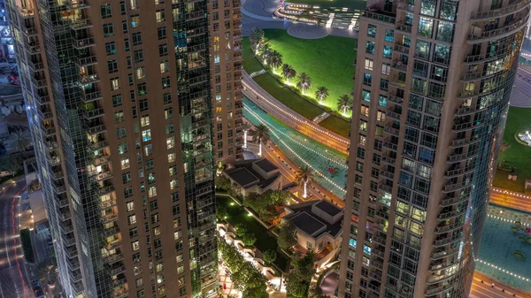 靠近喷泉的绿色草坪的公园使空中夜间的时间消逝 迪拜市中心人工湖的两座塔之间的景观 从上面俯瞰 有棕榈和树木 — 图库照片