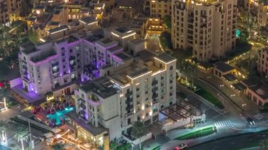 Gökyüzü manzarası, eski kasaba adasının aydınlatılmış geleneksel küçük evlerinin gece zaman çizelgesine yukarıdan bakıyor. Dubai şehir merkezinde sokak trafiği ve ağaçlarla