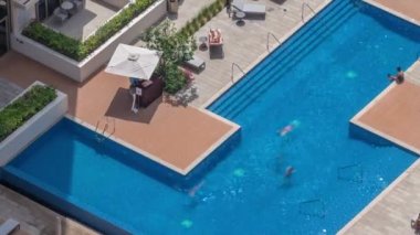 Çatıdaki yüzme havuzu yukarıdan izleniyor, insanların yüzdüğü ve şemsiyelerin altında dinlendiği bir havuz. Hareket eden gölgeler