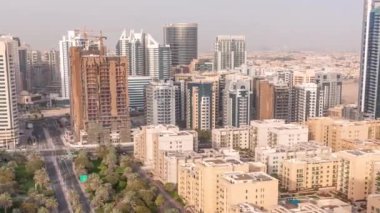 Barsha Heights bölgesindeki gökdelenler ve Greenens bölgesindeki alçak binalar. Kavşağı olan yol kenarında palmiyeler ve ağaçlarla Dubai silüeti