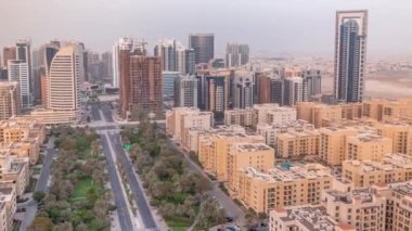 Barsha Heights bölgesindeki gökdelenler ve Greenens bölgesindeki alçak binalar. Palmiyeler ve ağaçlarla çevrili bir yolda Dubai silüeti
