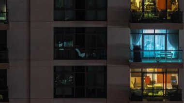Gece saatlerinde apartmanın pencereleri, balkonunda sandalyeleri olan aydınlık evlerin ışıkları. Gökdelenlerin kentsel manzarası