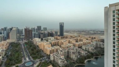 Barsha Heights bölgesindeki gökdelenler ve Greenens bölgesindeki alçak binalar hava gününden geceye geçiş zamanları. Dubai silueti, palmiyeler ve havuz üzerindeki çeşme.