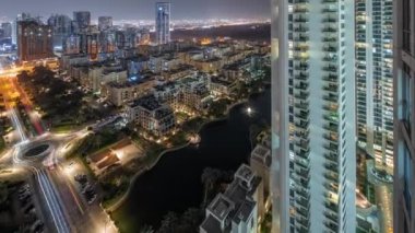 Yeşiller Bölgesi 'ndeki havuz ve alçak binalar gece uçuşları. Arka planda Barsha Heights bölgesinde gökdelenleri olan Dubai gökdelenleri