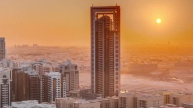 Barsha Heights bölgesindeki gökdelenler ve Greenens bölgesindeki alçak binalar üzerinde gün doğumu. Dubai silueti, turuncu gökyüzü ve arkaplanda çöl.